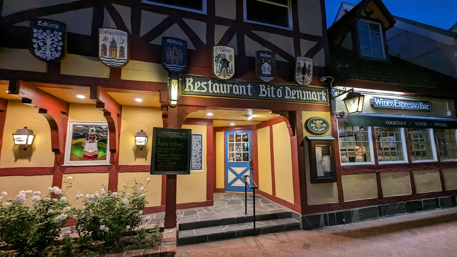 Evening exterior of Bit O'Denmark Restaurant with an illuminated sign and blue entrance door